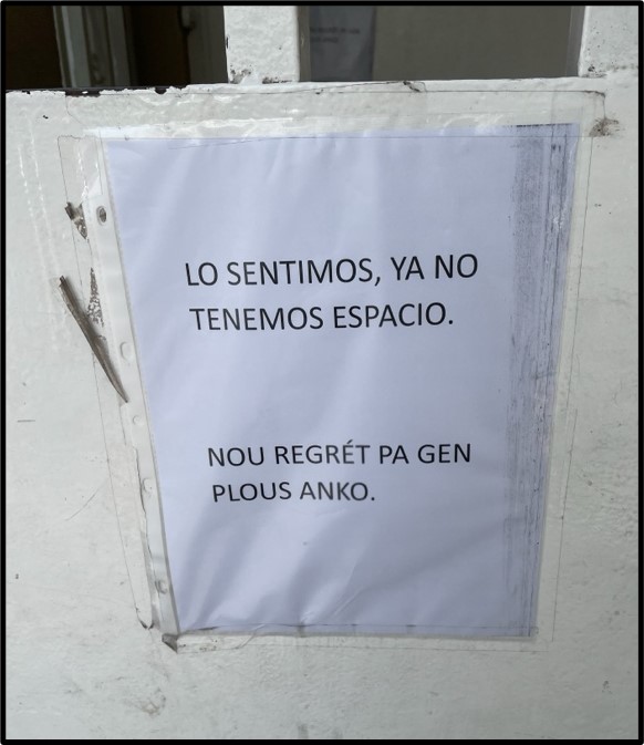 A sign on white copy-paper, taped to a white surface, reads in Spanish: “Lo sentimos, ya no temenos espacio” and in Haitian Creole” “Nou regret pa gen plous anko.”
